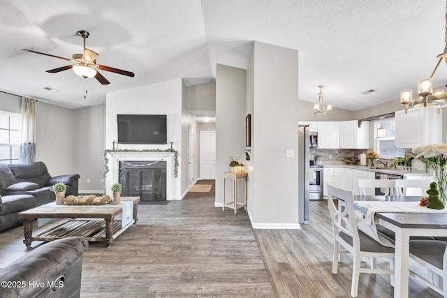 living area featuring visible vents, lofted ceiling, a fireplace with flush hearth, ceiling fan with notable chandelier, and light wood-type flooring