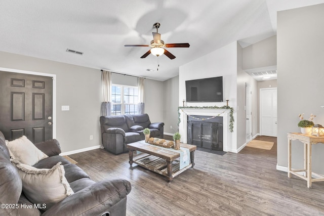 living area with visible vents, ceiling fan, a fireplace with flush hearth, vaulted ceiling, and wood finished floors