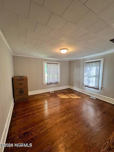unfurnished room featuring crown molding, baseboards, and dark wood-type flooring