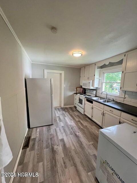 kitchen featuring white appliances, wood finished floors, crown molding, and a sink