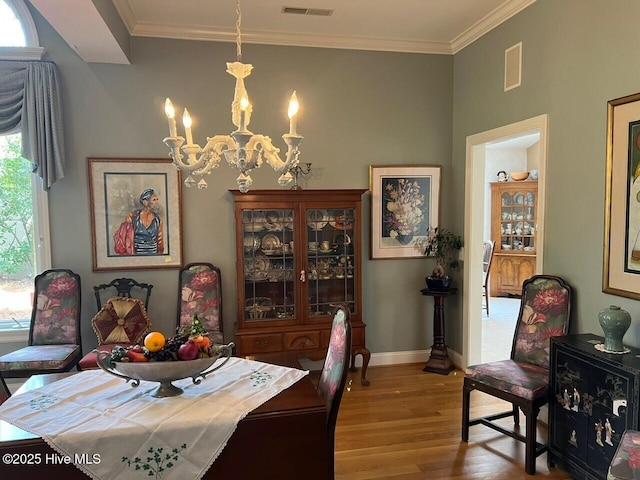 dining space with an inviting chandelier, crown molding, wood finished floors, and visible vents