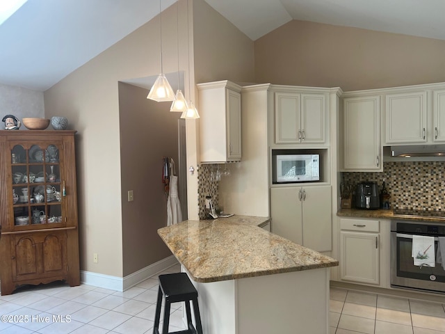 kitchen featuring white microwave, oven, under cabinet range hood, lofted ceiling, and light tile patterned floors