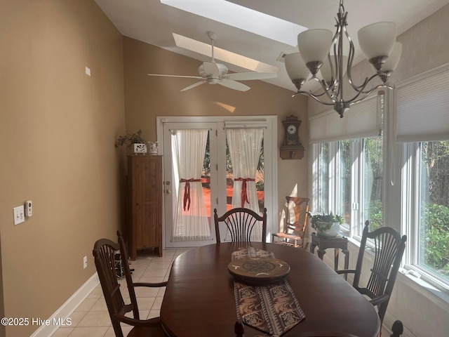 dining area with light tile patterned flooring, ceiling fan with notable chandelier, lofted ceiling with skylight, and baseboards