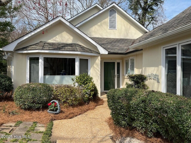 doorway to property with stucco siding and roof with shingles