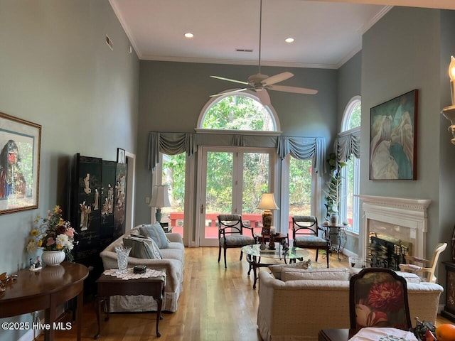 living area featuring wood finished floors, crown molding, a ceiling fan, and a high end fireplace