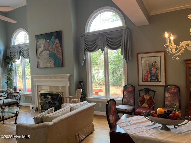 living area with ornamental molding, light wood-style floors, a fireplace, baseboards, and a towering ceiling