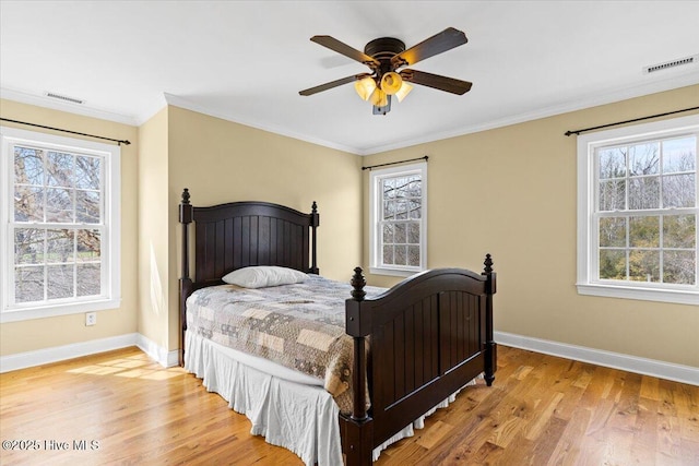 bedroom featuring baseboards, wood finished floors, visible vents, and ornamental molding