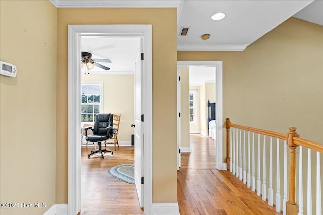 hallway with baseboards, visible vents, ornamental molding, light wood-style floors, and an upstairs landing