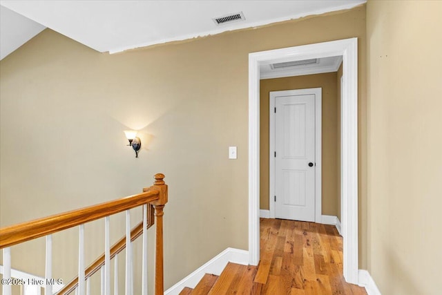 hallway featuring an upstairs landing, visible vents, baseboards, and wood finished floors