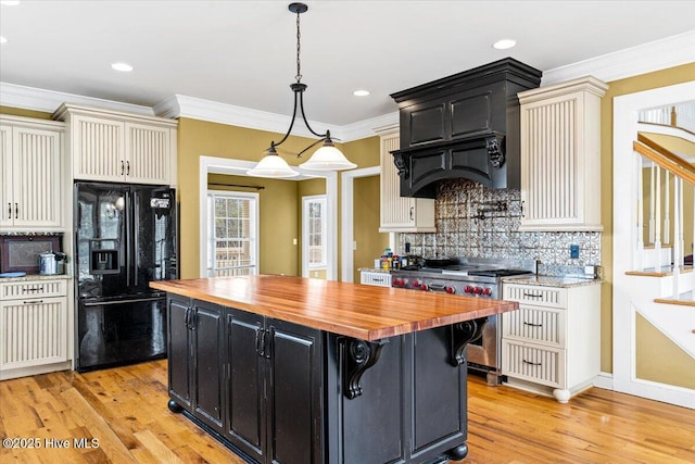 kitchen featuring stainless steel range with gas cooktop, a kitchen island, black fridge, dark cabinets, and butcher block counters