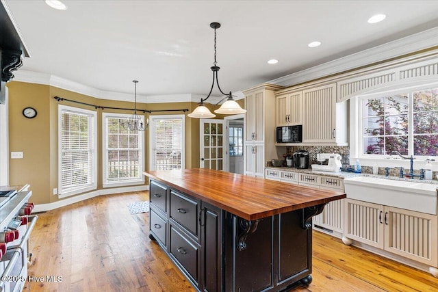 kitchen with wooden counters, a sink, ornamental molding, black microwave, and cream cabinets