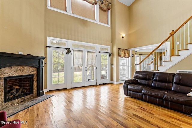 living room with stairway, wood-type flooring, french doors, a fireplace, and a towering ceiling