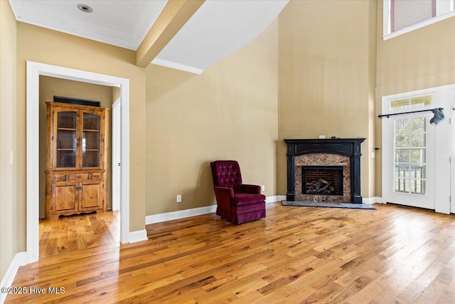 unfurnished room featuring light wood-style floors, crown molding, a premium fireplace, baseboards, and a towering ceiling