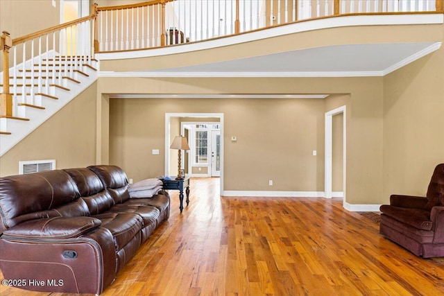 living area with visible vents, ornamental molding, wood-type flooring, a high ceiling, and baseboards