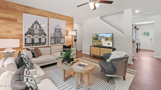 living area with visible vents, wood finished floors, wood walls, baseboards, and ceiling fan