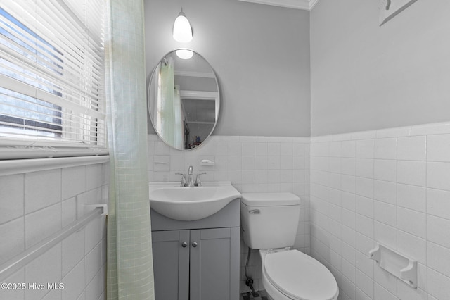 half bathroom featuring tile walls, a wainscoted wall, toilet, and vanity