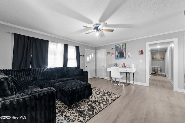 living area featuring baseboards, light wood-style flooring, ceiling fan, a textured ceiling, and crown molding