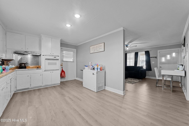 kitchen with oven, a ceiling fan, under cabinet range hood, white cabinets, and crown molding