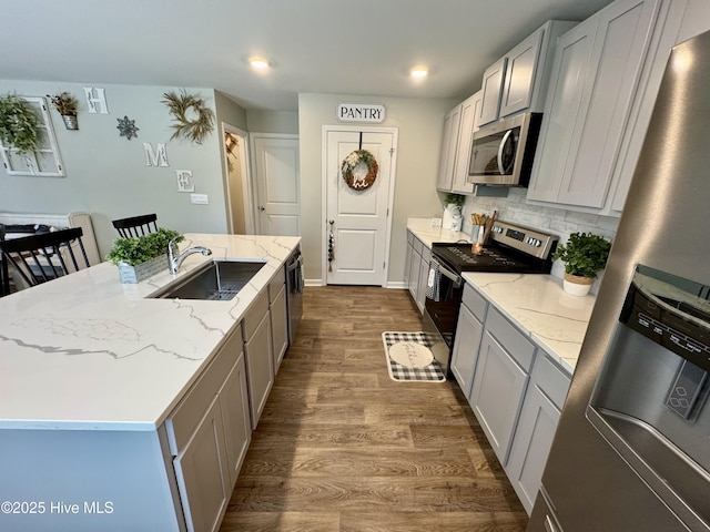 kitchen with a sink, light stone counters, backsplash, dark wood-style floors, and stainless steel appliances