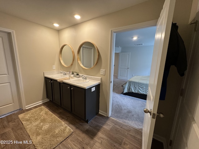 bathroom featuring wood finished floors, baseboards, visible vents, double vanity, and a sink