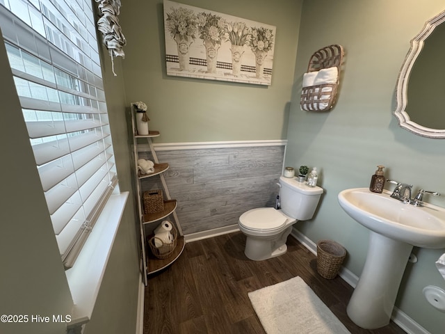 half bathroom with wooden walls, wood finished floors, a wainscoted wall, baseboards, and toilet