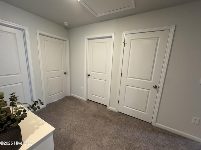 unfurnished bedroom with dark carpet, attic access, and baseboards