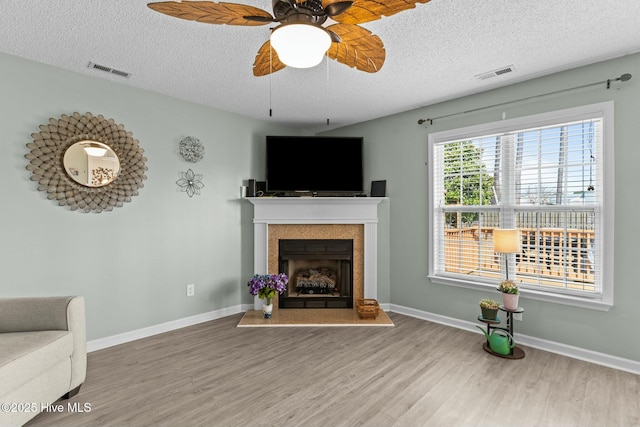 living area with a textured ceiling, wood finished floors, visible vents, and a fireplace with raised hearth