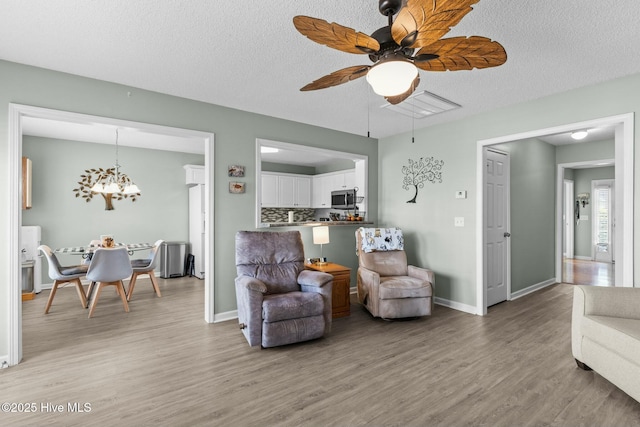 living area featuring ceiling fan with notable chandelier, a textured ceiling, light wood-type flooring, and baseboards