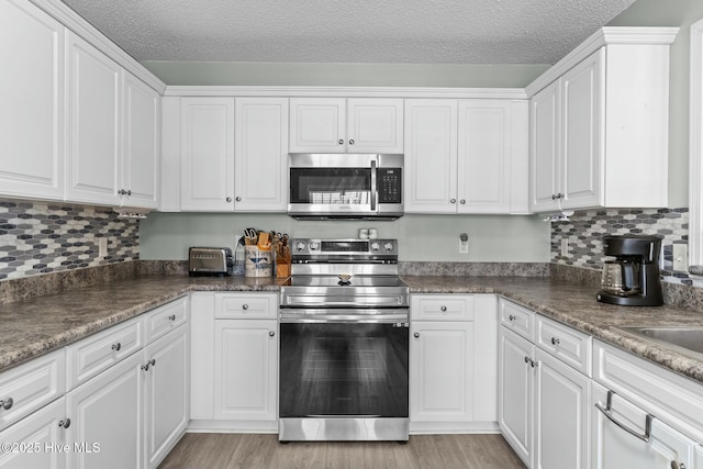 kitchen featuring light wood finished floors, backsplash, stainless steel appliances, white cabinets, and a textured ceiling