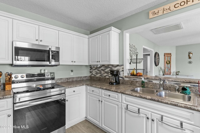 kitchen with a textured ceiling, white cabinets, appliances with stainless steel finishes, and a sink