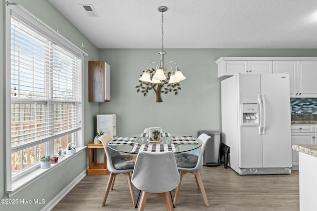 dining space with visible vents, light wood-style floors, a chandelier, and a textured ceiling