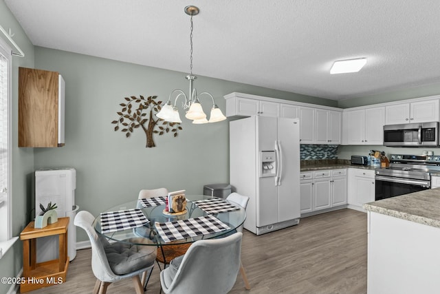 kitchen featuring light wood-type flooring, stainless steel appliances, an inviting chandelier, and white cabinets