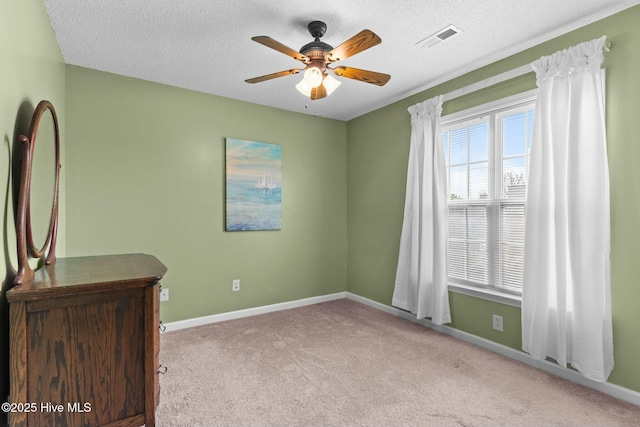 carpeted spare room with visible vents, a textured ceiling, baseboards, and a ceiling fan