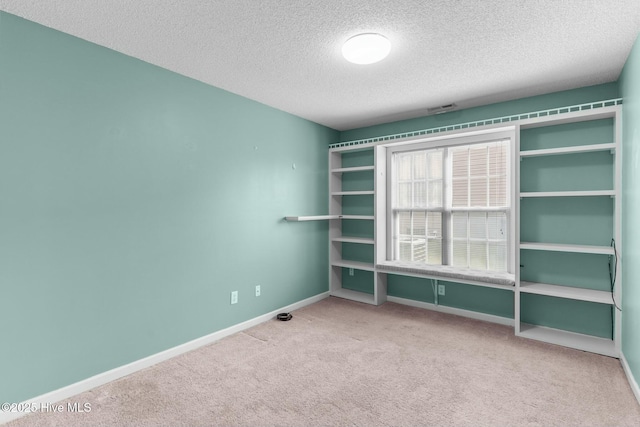 carpeted spare room featuring visible vents, a textured ceiling, and baseboards