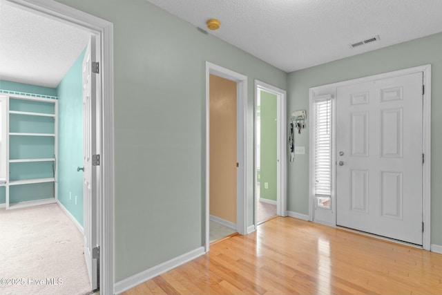 foyer entrance featuring visible vents, a textured ceiling, light wood-type flooring, and baseboards