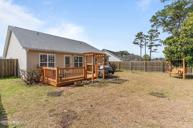 back of property with a yard, a deck, a fenced backyard, and a shingled roof