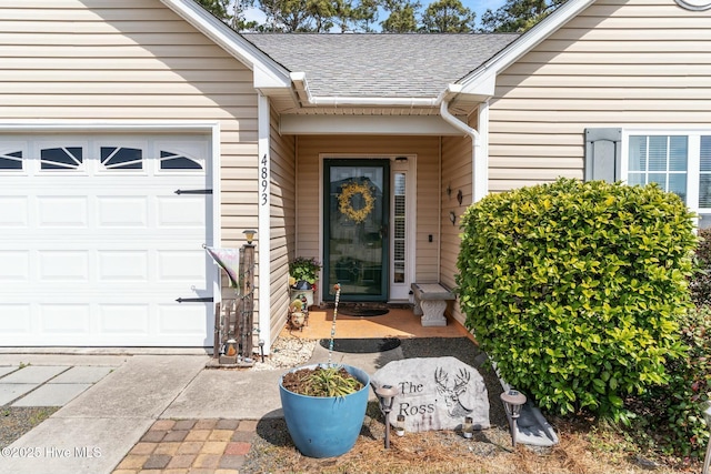 entrance to property featuring a garage and roof with shingles