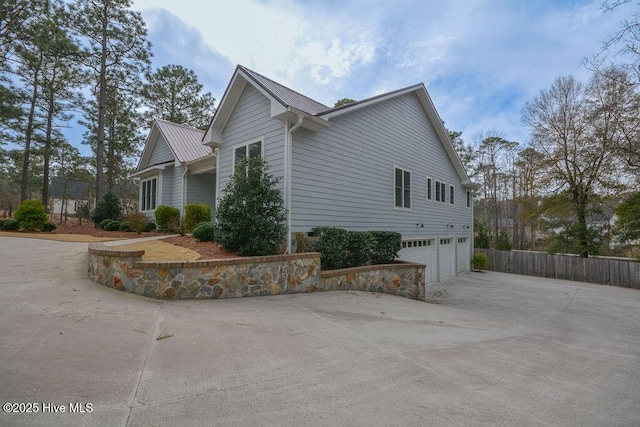 view of property exterior featuring fence, a garage, driveway, and metal roof