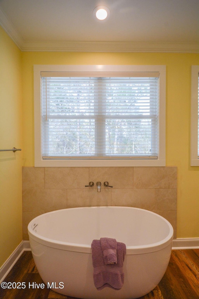 full bath with ornamental molding, wood finished floors, baseboards, and a freestanding bath