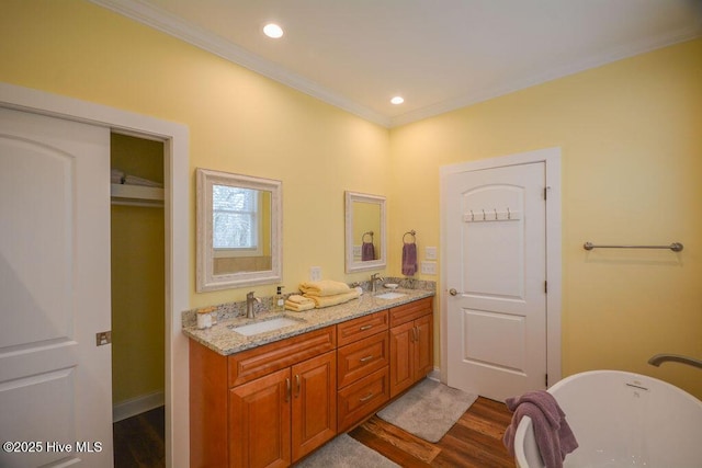 full bathroom featuring wood finished floors, double vanity, a freestanding tub, ornamental molding, and a sink