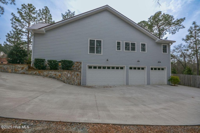 view of side of home with concrete driveway, fence, a garage, and metal roof