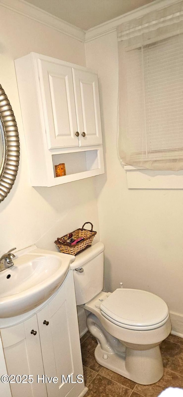 half bathroom with baseboards, vanity, toilet, and crown molding