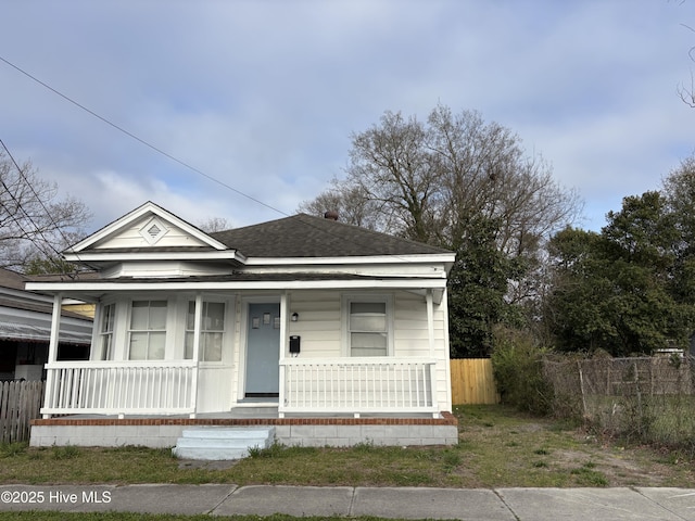 view of front of home featuring covered porch, roof with shingles, and fence