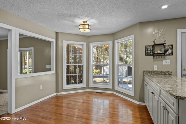 dining space with light wood-style flooring, baseboards, visible vents, and a textured ceiling