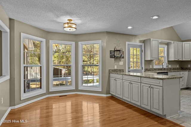 kitchen with stone counters, visible vents, baseboards, and a peninsula