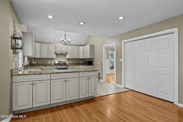 kitchen featuring under cabinet range hood, a chandelier, light stone counters, and stainless steel range with gas stovetop