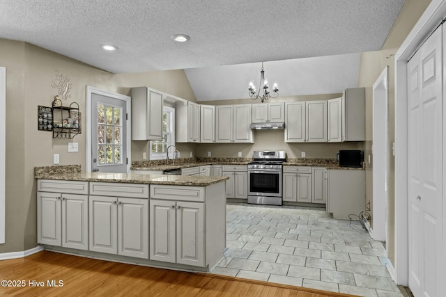 kitchen with stone countertops, under cabinet range hood, gas stove, a peninsula, and an inviting chandelier