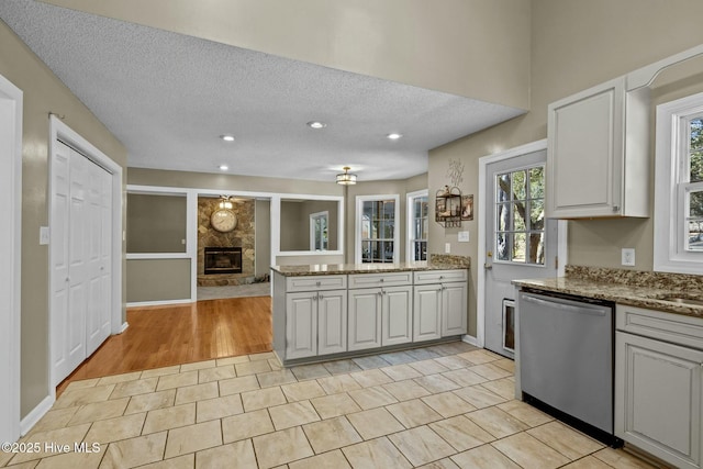 kitchen featuring stone countertops, stainless steel dishwasher, a textured ceiling, a stone fireplace, and a peninsula