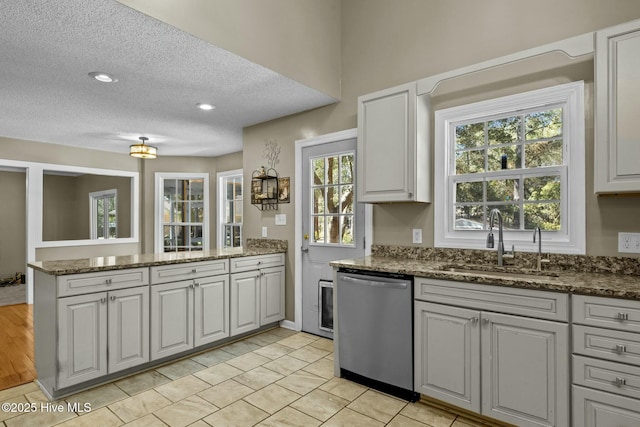 kitchen featuring dark stone countertops, a peninsula, stainless steel dishwasher, a textured ceiling, and a sink