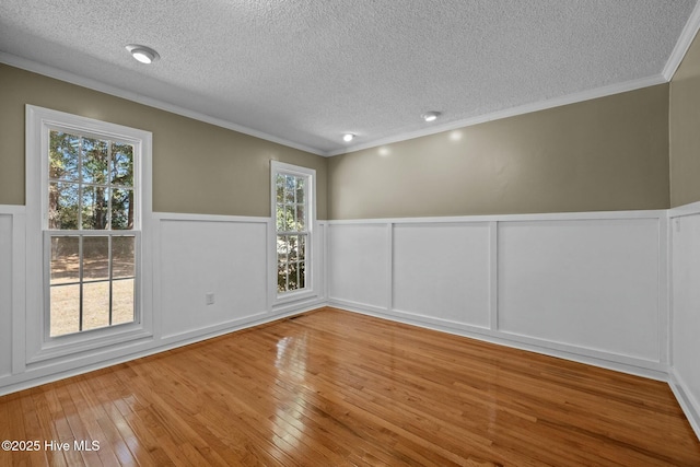 unfurnished room with a wainscoted wall, a textured ceiling, hardwood / wood-style floors, crown molding, and a decorative wall